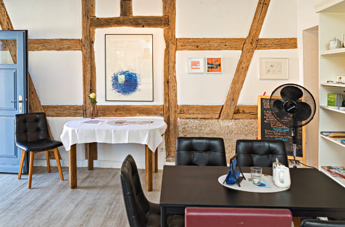 Gemütlicher Innenraum des Bürgercafés Ummerstadt mit Fachwerkbalken, Tischen, Stühlen und Kunstwerken an den Wänden.
