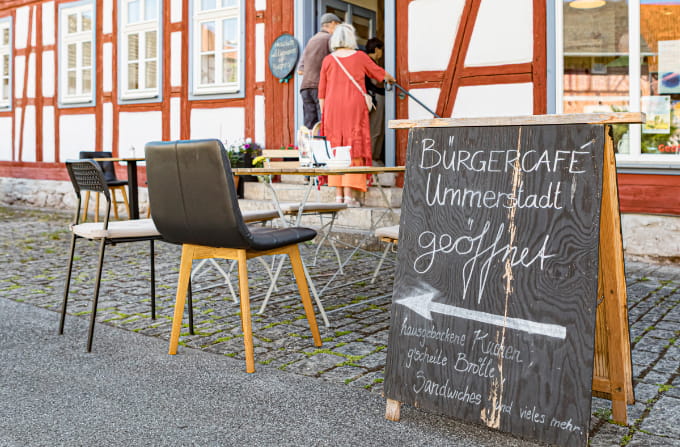 Aufsteller vor dem Bürgercafé Ummerstadt mit Sitzplätzen im Außenbereich.