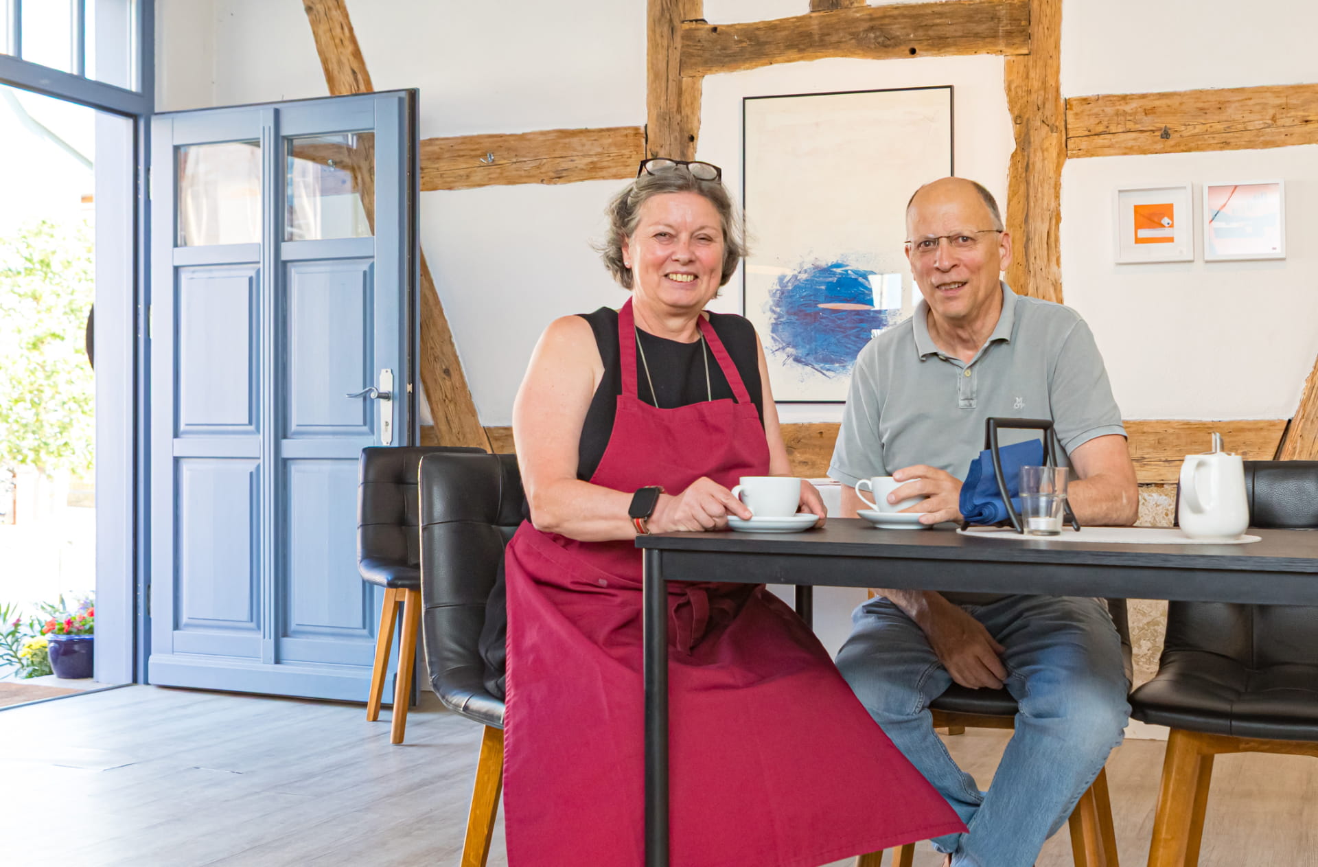 Die Besitzer des Bürgercafés Ummerstadt sitzen mit Kaffeetassen an einem Tisch im gemütlichen Fachwerk-Innenraum.